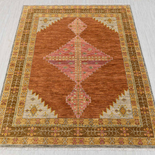 Hand-knotted rug in rust, pink, and gold with large geometric diamond medallion design.