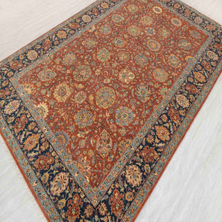 Hand-knotted wool rug featuring dense allover floral pattern in rust field with navy and light blue border, 6x9 ft