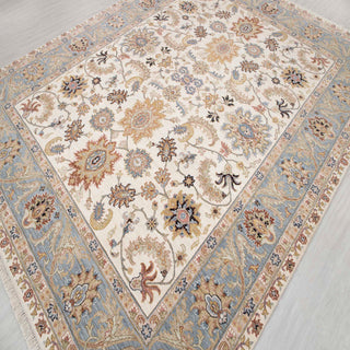 Hand-knotted wool rug featuring intricate botanical pattern in soft ivory field with light blue border, 8x10 ft.
