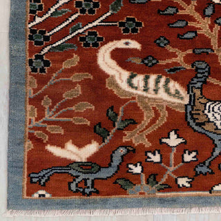 Modern hand-knotted rug with detailed nature scene pattern in rust, gray-blue, beige tones.

