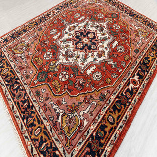 Modern hand-knotted rug with graphic medallion layout and angular motifs in rust, navy, rose and cream tones.
