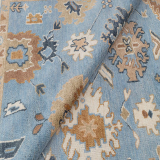 Turkish Oushak-style hand-knotted rug with soft blue field and ivory floral border motif.